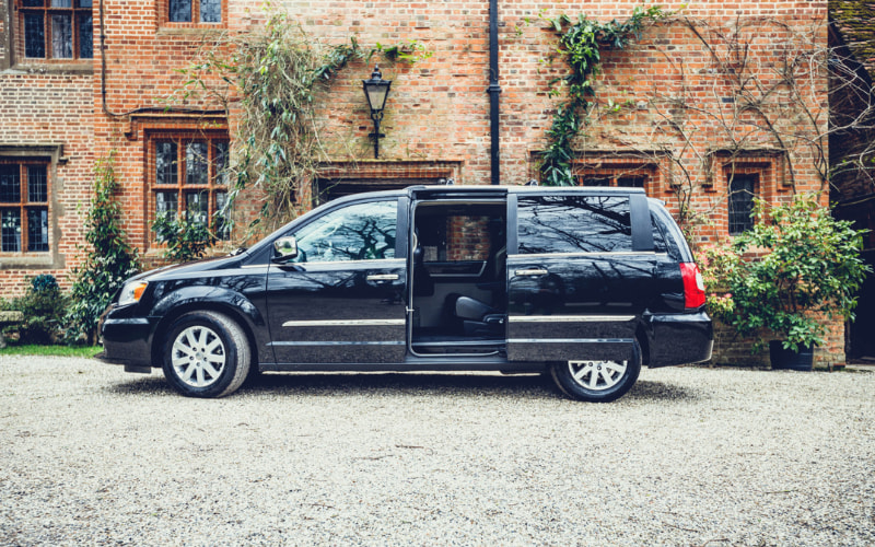 Black vehicle parked on gravel in front of large brick house with door open