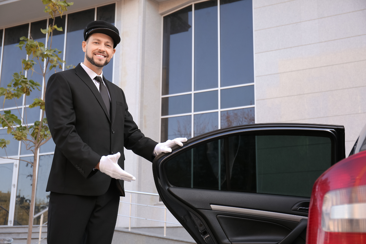 Chauffeur smiling, holding the door and showing the passenger to their seat